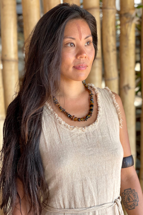 Model wearing a hand polished dark amber necklace on a natural linen dress, warm earthy tones.